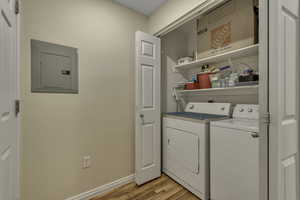 Laundry room with electric panel, light wood finished floors, and washing machine and dryer
