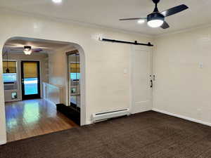 Empty room featuring a ceiling fan, a textured wall, crown molding, arched walkways, and a baseboard heating unit