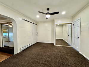 Unfurnished bedroom with a textured wall, ornamental molding, arched walkways, a closet, and baseboard heating