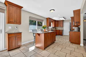 Kitchen with dark stone counters, brown cabinets, a kitchen bar, decorative backsplash, and a center island