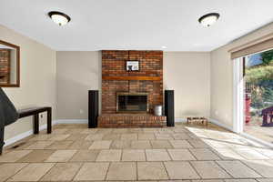 Unfurnished living room featuring a brick fireplace and baseboards