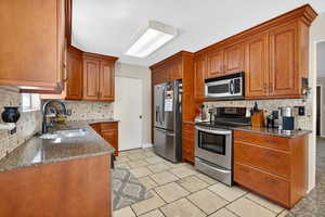 Kitchen with dark stone countertops, tasteful backsplash, appliances with stainless steel finishes, and brown cabinetry