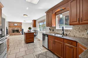 Kitchen featuring brown cabinets, dark stone counters, a fireplace, appliances with stainless steel finishes, and a textured ceiling