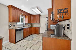 Kitchen with tasteful backsplash, brown cabinetry, dark stone counters, stainless steel dishwasher, and electric range