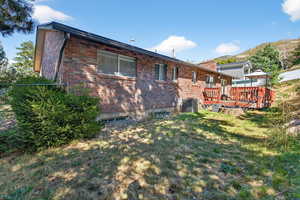 Back of house with brick siding, a deck with mountain view, a lawn, and a chimney