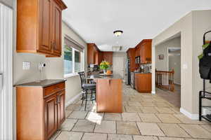 Kitchen with dark stone countertops, brown cabinetry, a breakfast bar area, stainless steel appliances, and stone tile floors