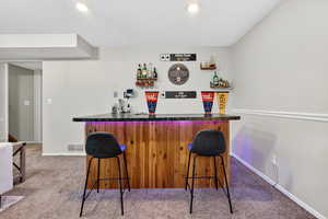 Indoor wet bar featuring dark countertops, light colored carpet, a textured ceiling, recessed lighting, and open shelves