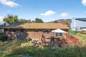 Back of property featuring brick siding, roof with shingles, a chimney, and a deck with mountain view
