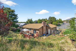 Back of property with a fenced backyard, brick siding, a deck, roof with shingles, and a chimney