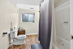 Full bath featuring shower / bath combo, light wood-style flooring, and a textured ceiling
