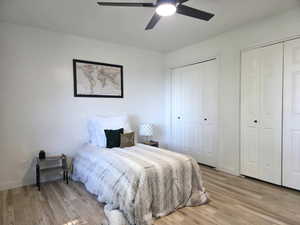 Bedroom with multiple closets, light wood-style flooring, and a ceiling fan