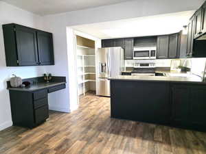 Kitchen with open shelves, appliances with stainless steel finishes, dark wood-style flooring, a peninsula, and dark cabinets
