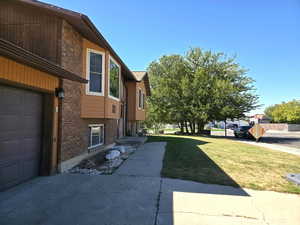 View of side of property featuring brick siding, a garage, and a lawn