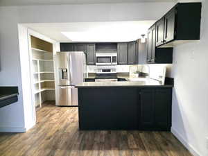 Kitchen with dark cabinetry, stainless steel appliances, open shelves, and dark wood-style floors
