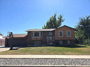 Bi-level home with concrete driveway, a front yard, an attached garage, and brick siding
