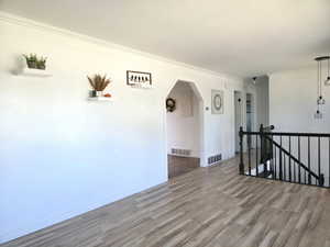 Spare room with arched walkways, wood finished floors, and ornamental molding