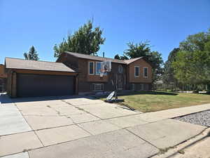 Raised ranch featuring driveway, a front lawn, a garage, and brick siding