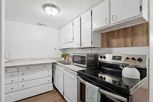 Kitchen with stainless steel appliances, light countertops, white cabinetry, and dark wood-style flooring