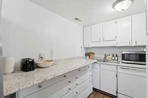 Kitchen featuring light countertops, white dishwasher, white cabinetry, stainless steel microwave, and dark wood-type flooring