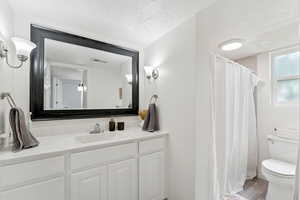 Bathroom with a textured ceiling, vanity, light wood-style floors, and a shower with curtain
