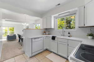 Kitchen featuring plenty of natural light, light colored carpet, white cabinets, and decorative light fixtures