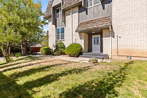 Property entrance with a yard, brick siding, and mansard roof