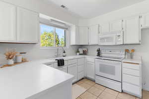 Kitchen with white appliances, white cabinets, light countertops, and light tile patterned floors