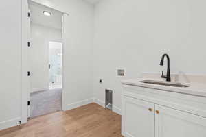 Laundry area with light wood-style floors, hookup for a washing machine, cabinet space, and electric dryer hookup