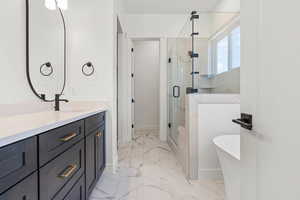 Full bath featuring a shower stall, a soaking tub, vanity, and light marble finish flooring