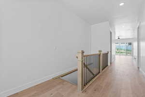 Hall with an upstairs landing, light wood-style floors, and recessed lighting