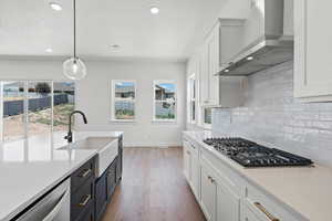 Kitchen with white cabinets, hanging light fixtures, light stone counters, wall chimney exhaust hood, and recessed lighting