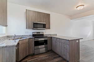 Kitchen with appliances with stainless steel finishes, a peninsula, light stone countertops, dark wood-type flooring, and modern cabinets