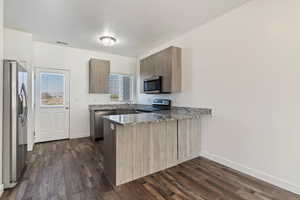 Kitchen featuring dark stone countertops, a peninsula, appliances with stainless steel finishes, dark wood-style floors, and modern cabinets