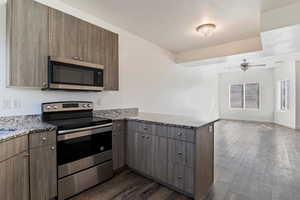 Kitchen featuring a peninsula, stainless steel appliances, dark wood-style flooring, light stone counters, and open floor plan