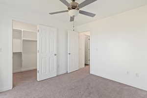 Unfurnished bedroom with light carpet, a walk in closet, and a ceiling fan
