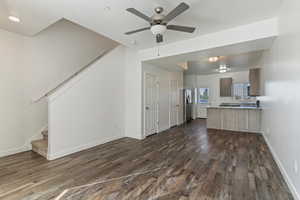 Unfurnished living room featuring stairs, dark wood-style flooring, and a ceiling fan