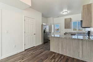 Kitchen featuring dark stone countertops, a peninsula, stainless steel fridge, dark wood-style flooring, and stove