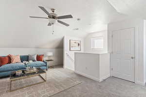 Sitting room featuring an upstairs landing, lofted ceiling, carpet flooring, a textured ceiling, and ceiling fan. Staged
