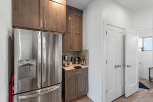 Kitchen featuring stainless steel fridge with ice dispenser, light countertops, decorative backsplash, light wood-style floors, and dark brown cabinets