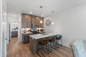 Kitchen with a breakfast bar area, pendant lighting, appliances with stainless steel finishes, light wood-type flooring, and light stone countertops