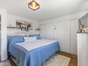 Primary bedroom featuring two closets, wood finished floors, and wood walls