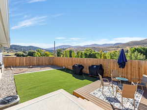 Fenced backyard with low maintenance artificial grass featuring a deck with mountain view and outdoor dining space