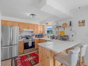 Kitchen with decorative backsplash, appliances with stainless steel finishes, light countertops, and a peninsula