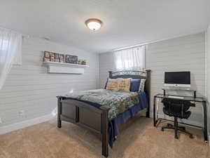 Carpeted bedroom with a textured ceiling, wood walls, and an office area
