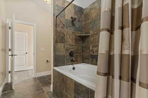 Bathroom with tiled shower / bath combo, stone tile flooring, and vaulted ceiling