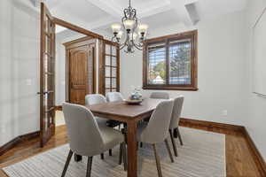 Dining area with beamed ceiling, coffered ceiling, wood finished floors, a chandelier, and french doors
