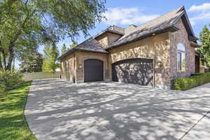 View of front of home with stucco siding, an attached garage, concrete driveway, stone siding, and a shingled roof