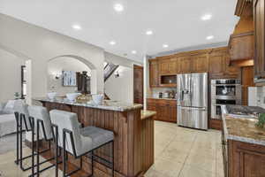 Kitchen featuring stainless steel appliances, decorative backsplash, light stone counters, recessed lighting, and brown cabinets