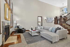 Living area with a towering ceiling, a high end fireplace, stairway, a chandelier, and wood finished floors