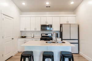 Kitchen featuring a kitchen breakfast bar, stainless steel appliances, light wood-type flooring, an island with sink, and white cabinetry